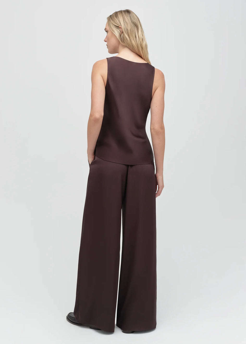 Woman wearing a brown sleeveless top and wide-leg pants on a white background