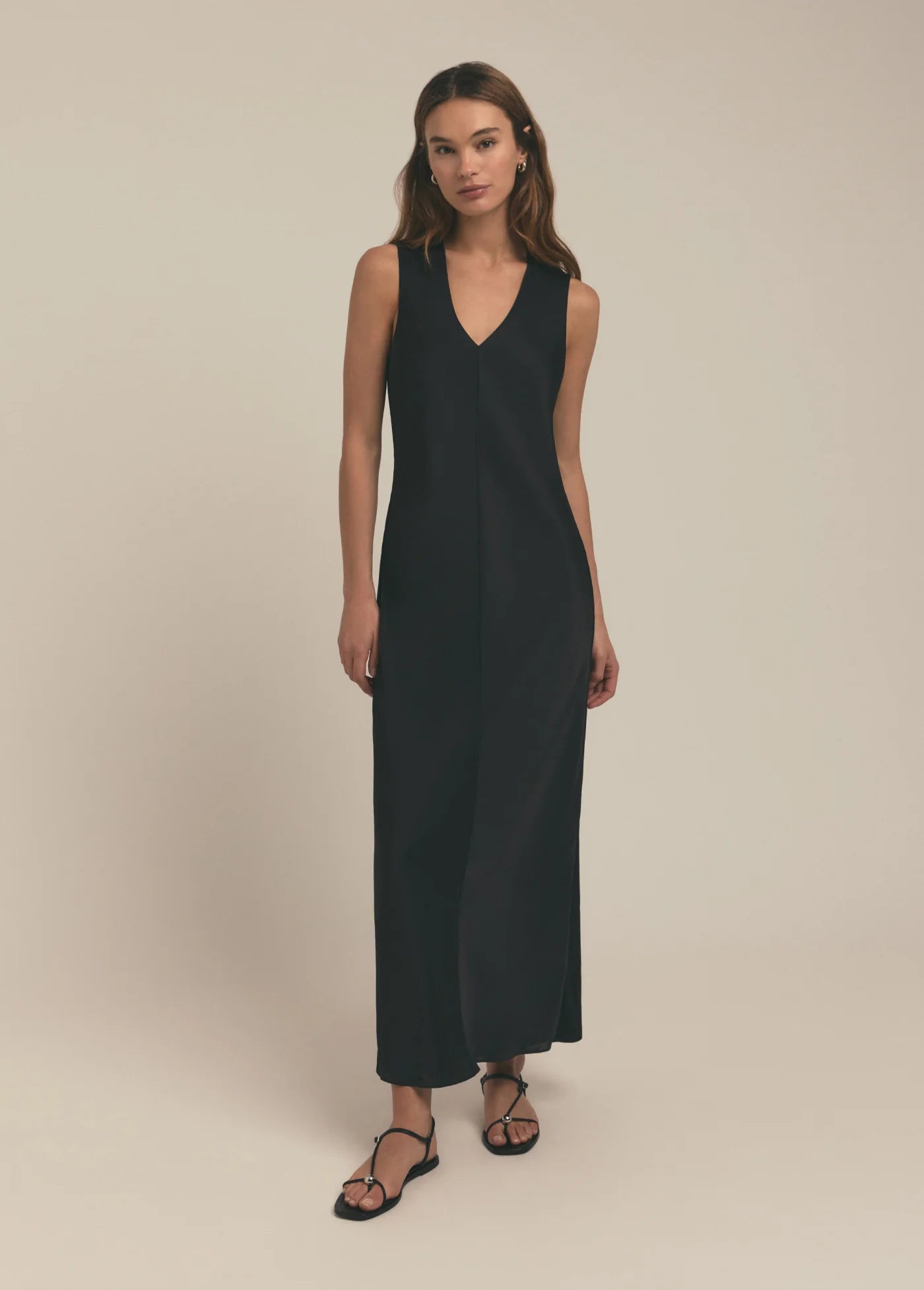 A woman standing in a studio setting, wearing a black sleeveless maxi dress with a V-neckline.