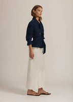 Woman wearing a navy blue jacket and white pants on a beige background