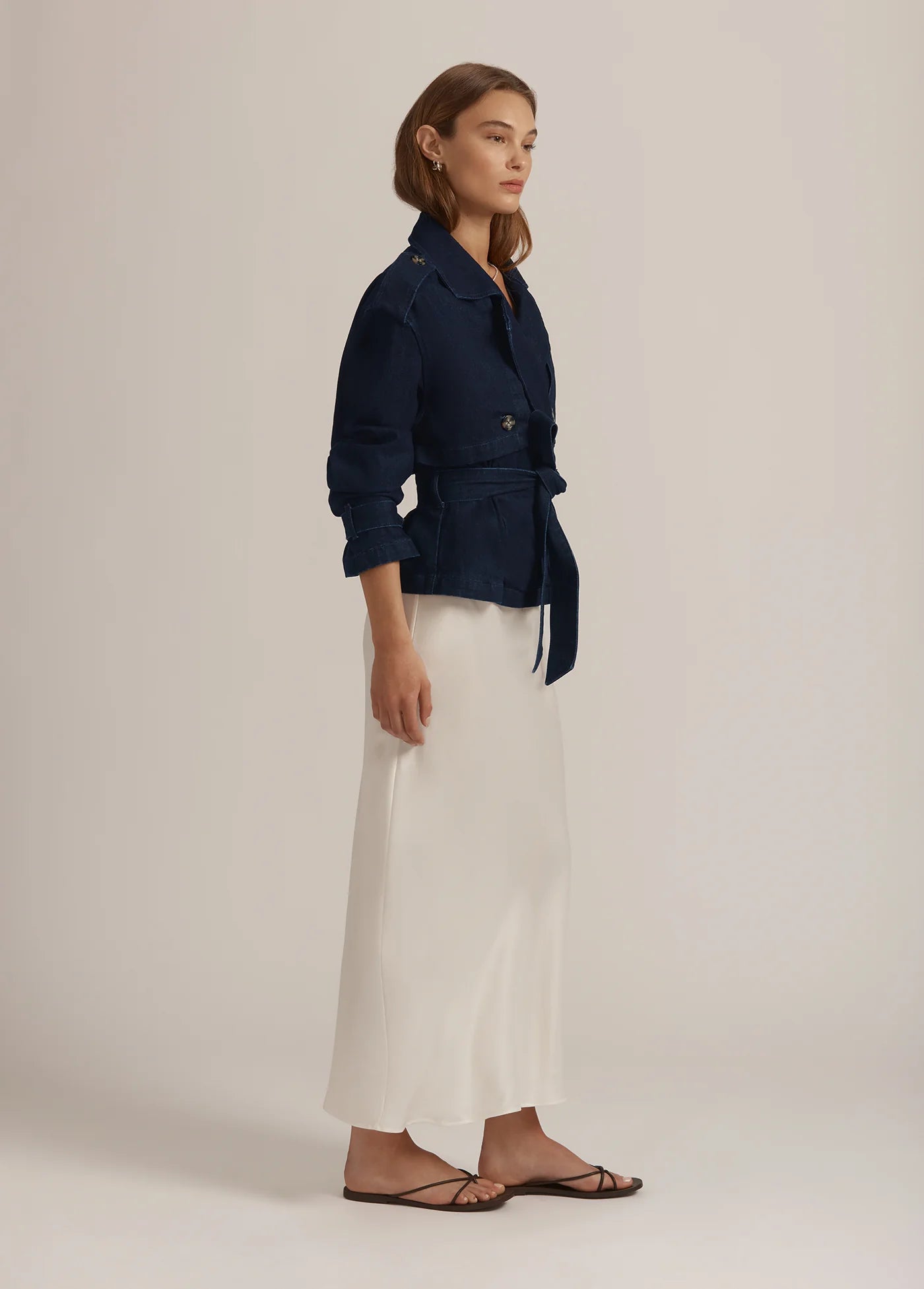 Woman wearing a navy blue jacket and white pants on a beige background