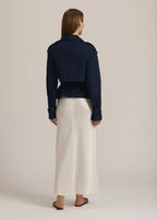 Person wearing a navy jacket and white pants on a beige background