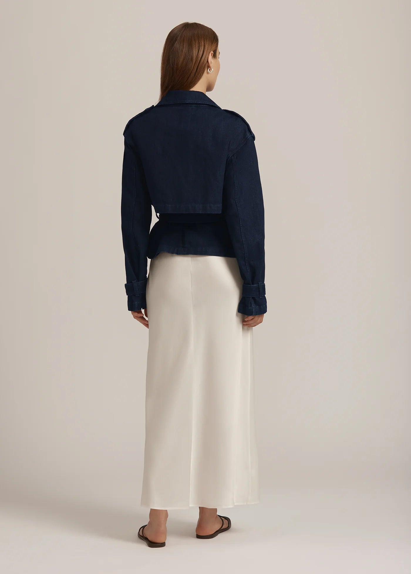 Person wearing a navy jacket and white pants on a beige background