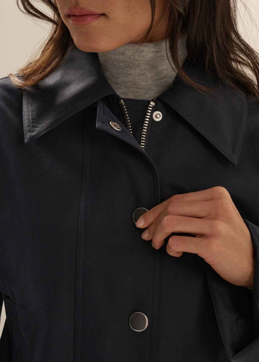 Person wearing a dark coat with buttons, focusing on the collar and buttons.
