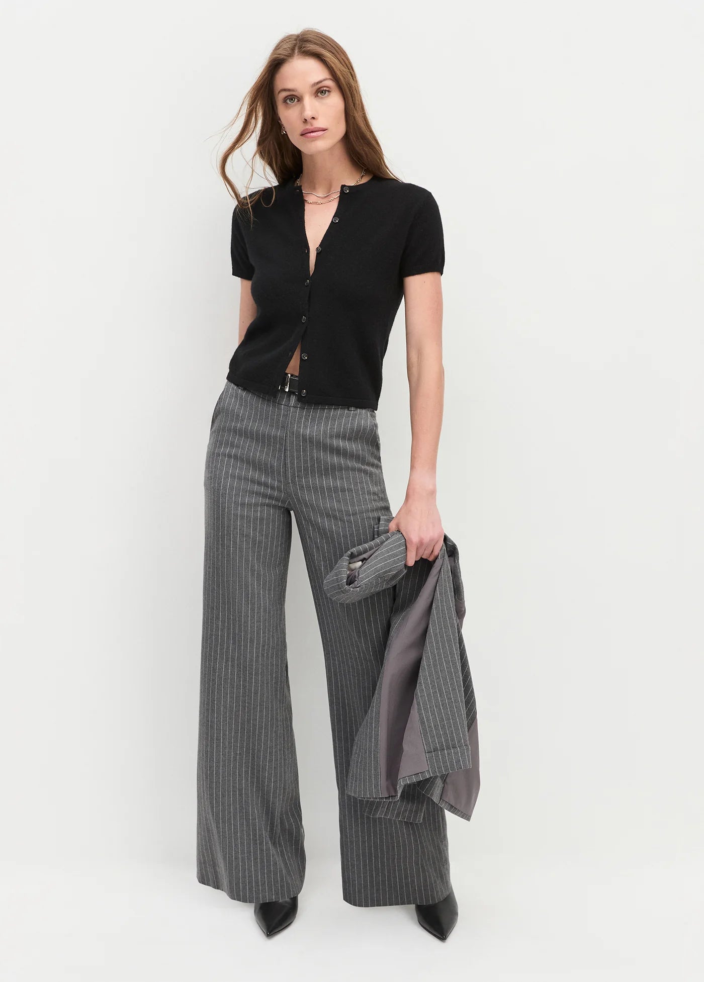 Woman wearing a black top and the jones  gray checkered pants by favourite daughter  holding a gray jacket on a white background