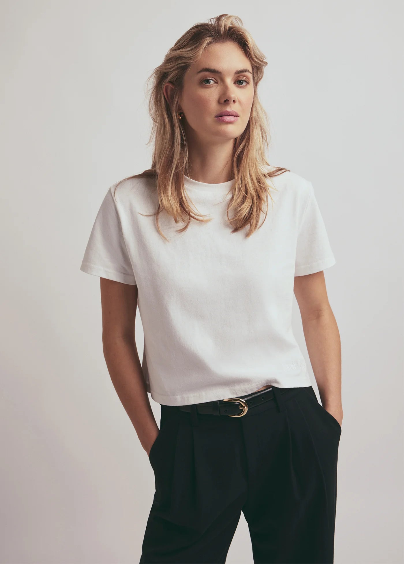 Woman wearing a white t-shirt and black pants against a plain background