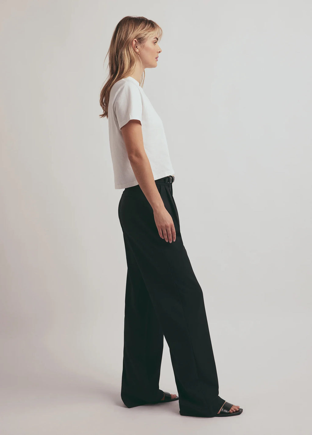 Woman wearing a white top and black pants on a plain background