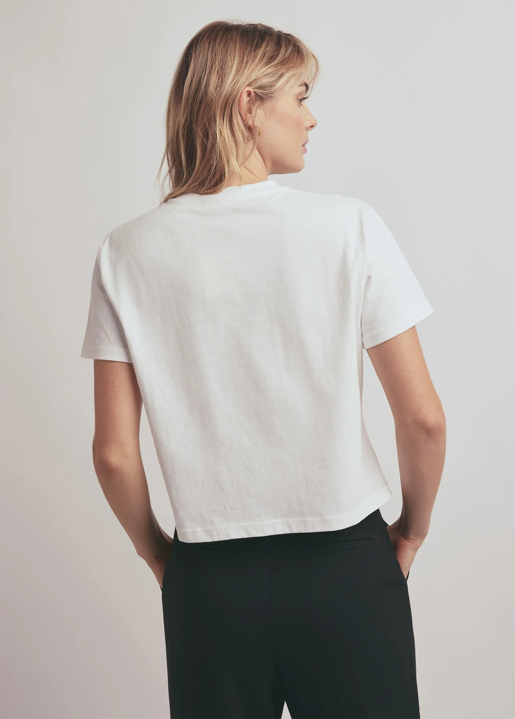 Person wearing a white t-shirt and black pants on a plain background