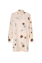 A long-sleeve button-up shirt dress in a light cream or pale beige color, decorated with a scattered floral print in muted red, green, and light blue tones, shown against a plain white background.