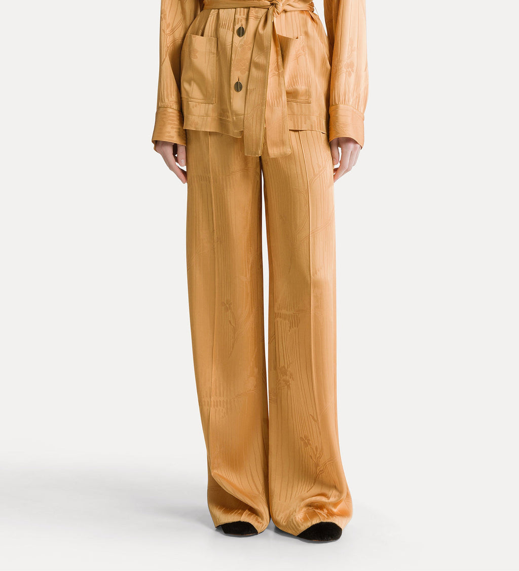 A model is shown from the waist down wearing a matching mustard yellow two-piece set consisting of a belted cropped jacket and wide-leg trousers, with a subtle vertical textured stripe pattern.