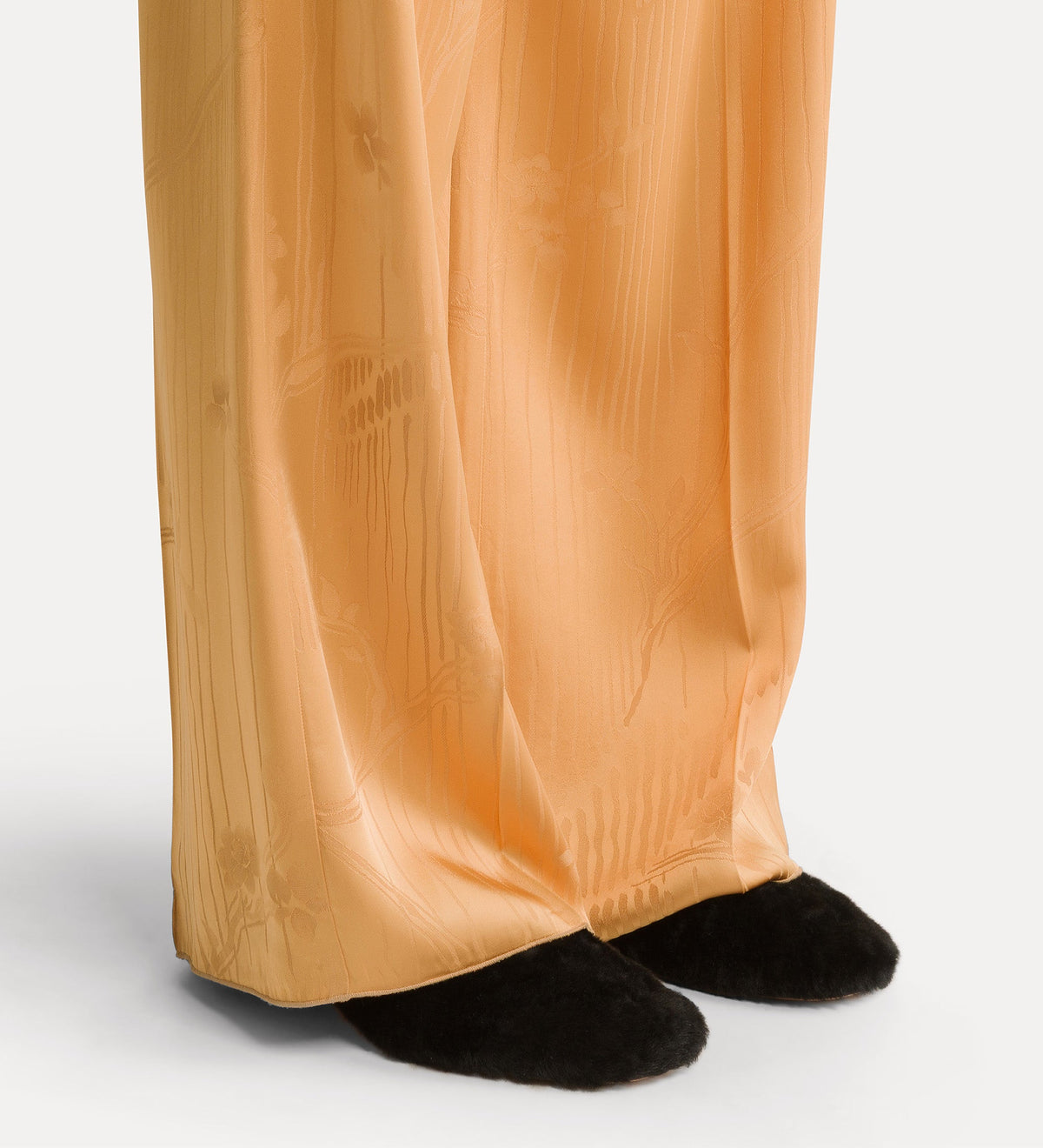 Close-up of a person wearing gold pants and black shoes on a white background