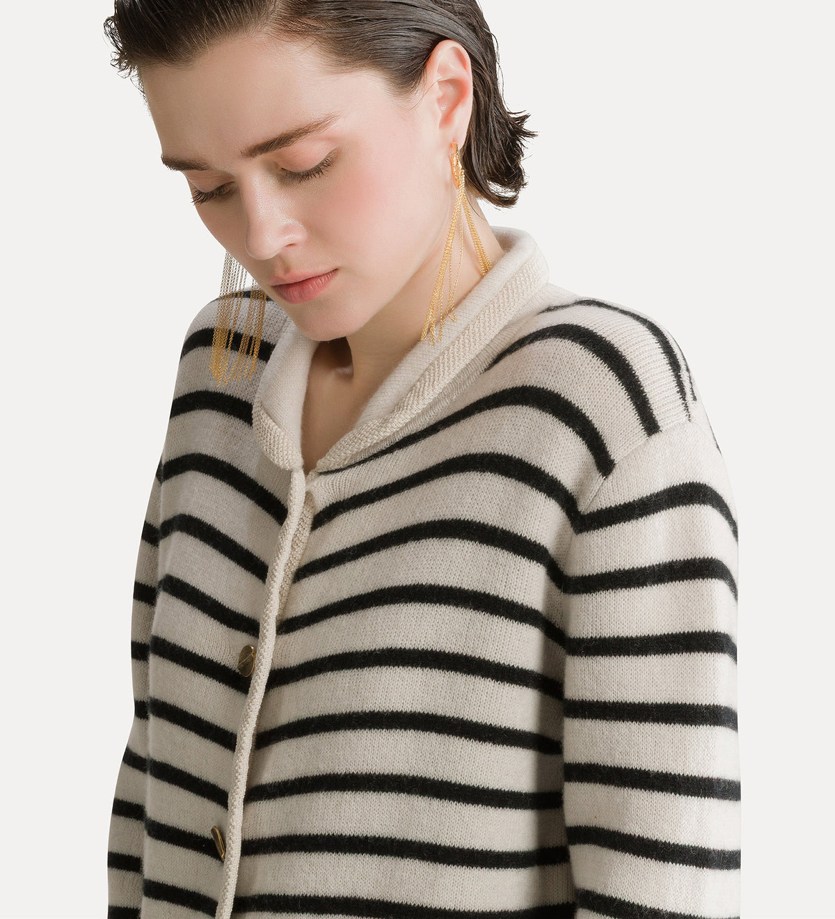 A close-up of a woman wearing a cream-colored knit cardigan with black horizontal stripes and a thick cream rope tie closure, set against a plain light background.
