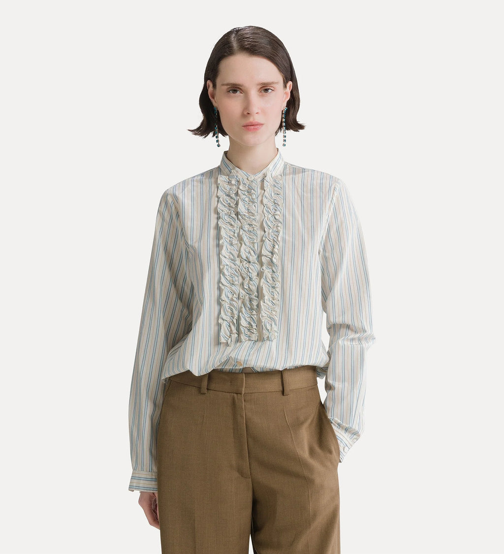 A model wearing a light blue and white vertically striped long-sleeve blouse with a prominent ruffled front panel, paired with brown trousers, against a light gray background.