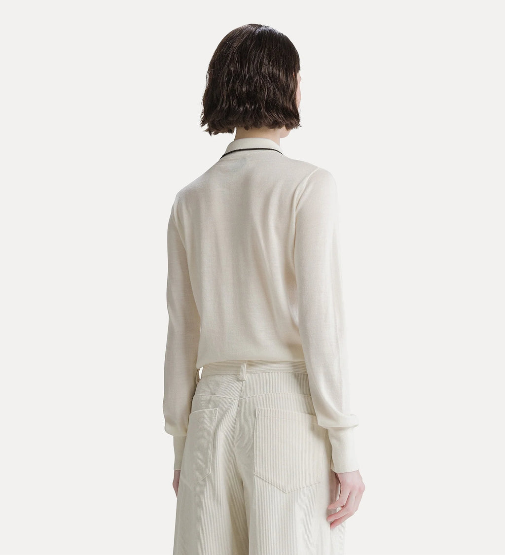 A model shown from the back wearing a cream-colored knit long-sleeve polo shirt with a thin black collar trim and matching cream trousers, set against a solid off-white background.