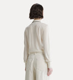 A model shown from the back wearing a cream-colored knit long-sleeve polo shirt with a thin black collar trim and matching cream trousers, set against a solid off-white background.