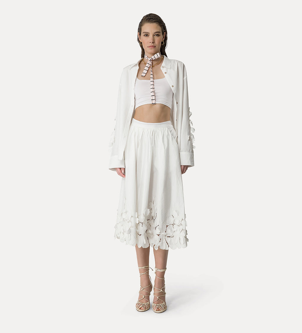 A model wearing a white long skirt with floral applique details and a matching top.