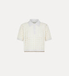 A woman wearing a white cropped polo shirt with geometric patterning and contrasting edges, paired with white trousers.