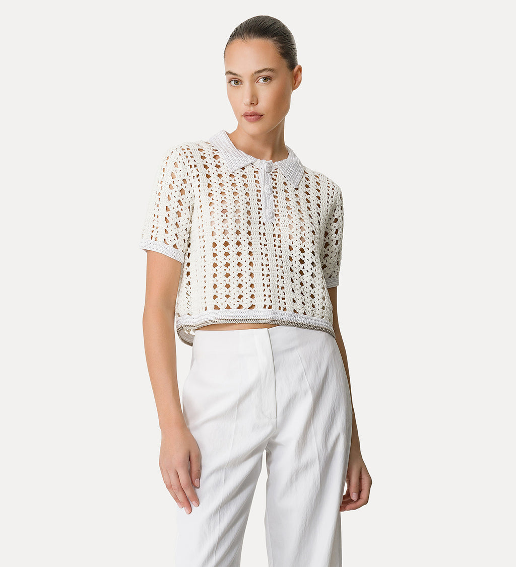 A woman wearing a white cropped polo shirt with geometric patterning and contrasting edges, paired with white trousers.