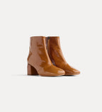 Pair of brown patent leather ankle boots on a light gray background