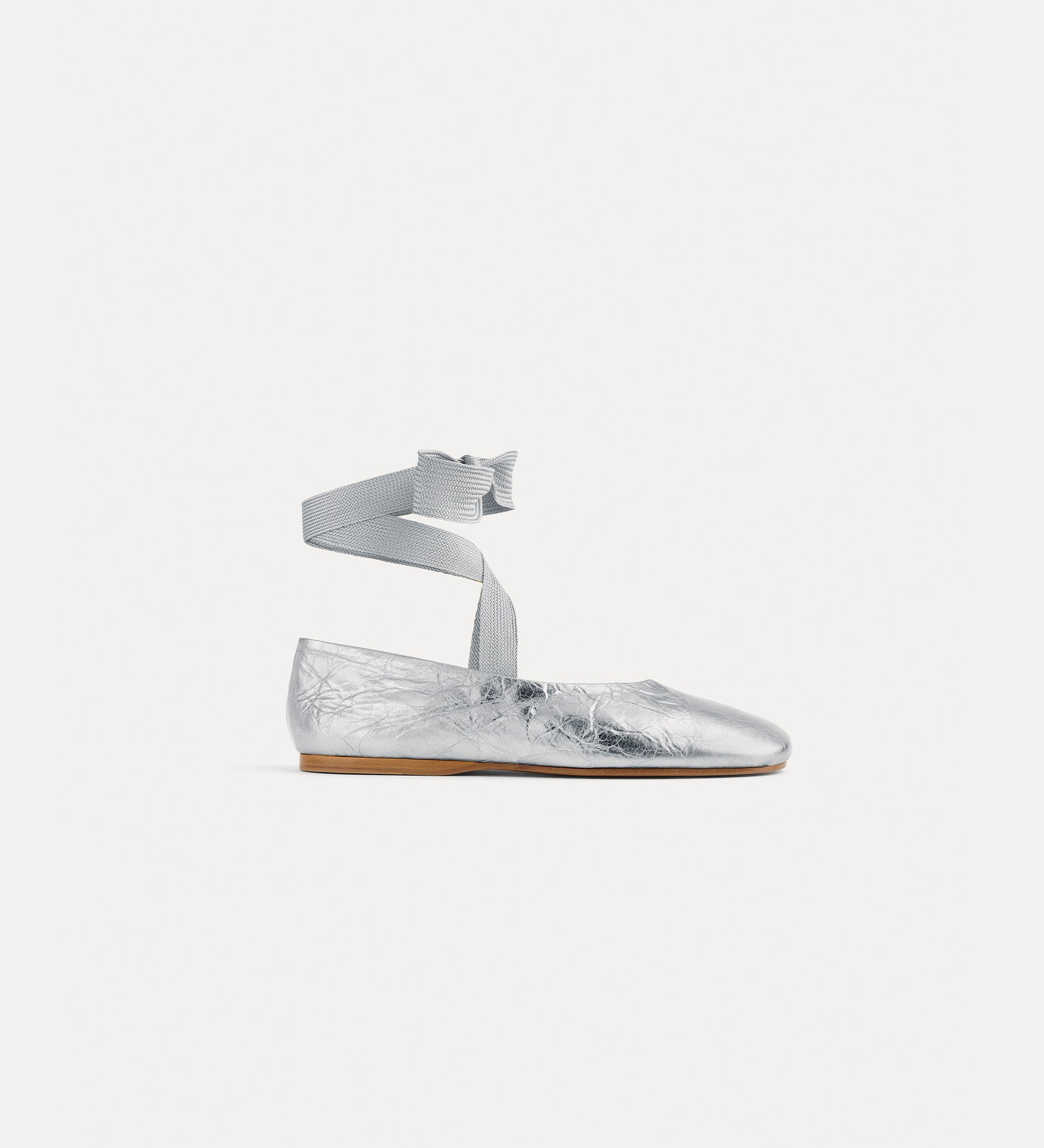 Silver flat shoe with ankle strap on a white background