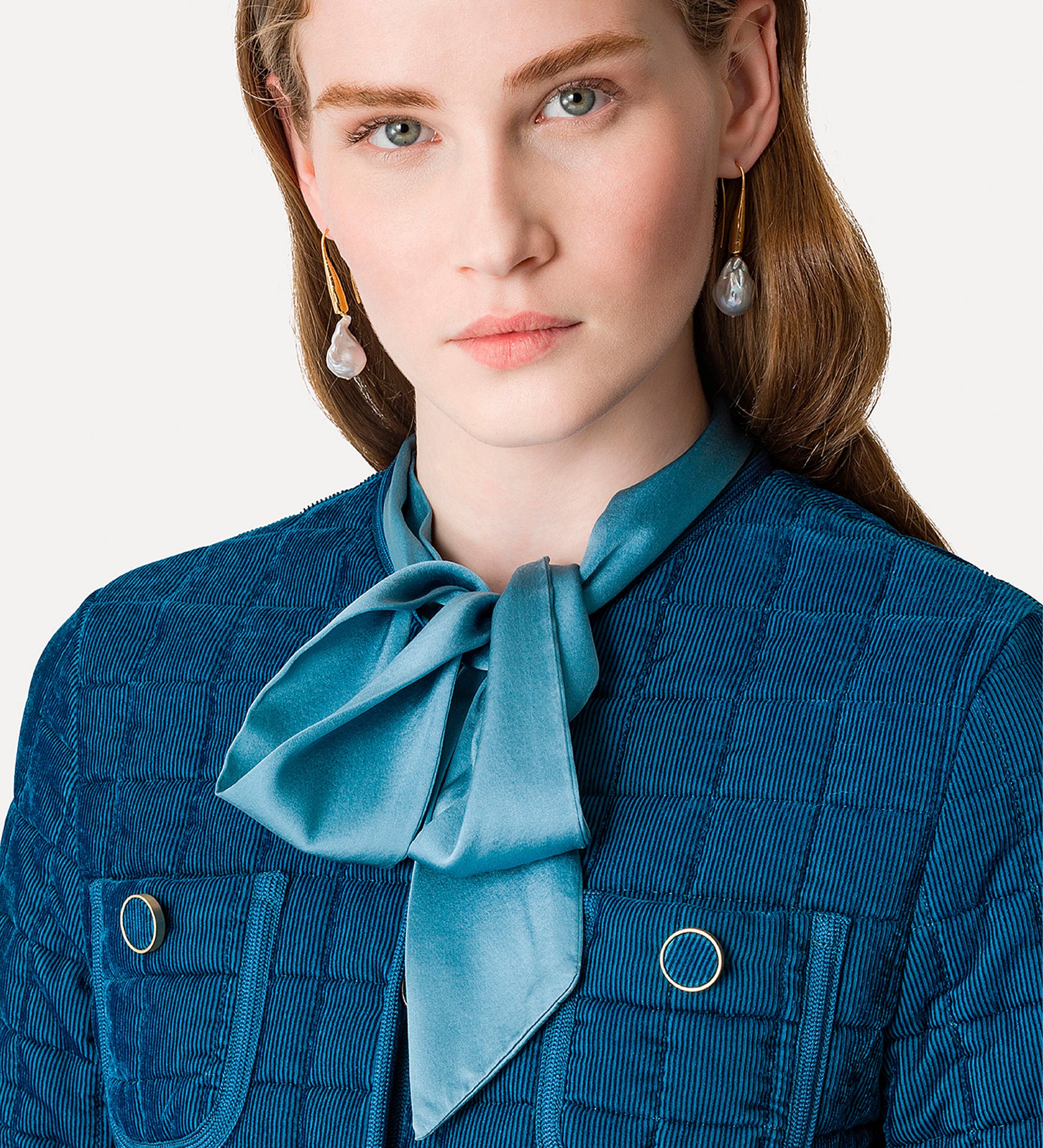 Woman wearing a blue jacket with a matching scarf against a plain background