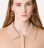 Woman wearing gold hoop earrings with pearl accents against a plain background