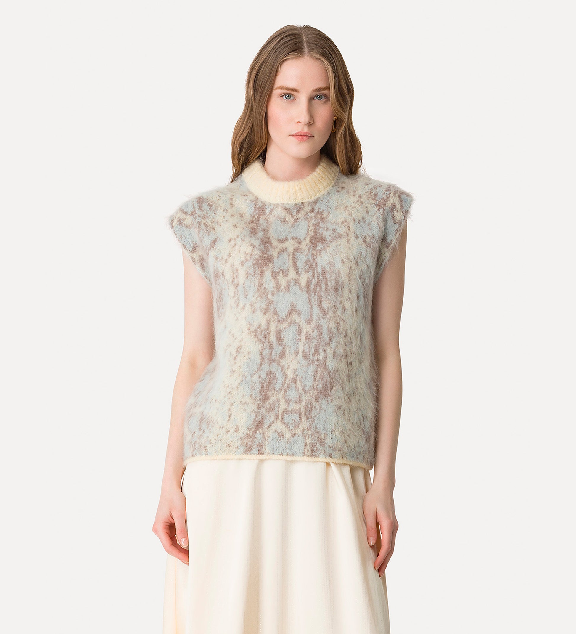 Woman wearing a patterned sleeveless top and white skirt on a plain background