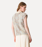 Woman wearing a patterned sleeveless top and beige pants on a white background