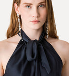 Woman wearing a black halter top with a bow and pearl earrings on a light background