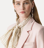 Woman wearing a pink coat, beige scarf, and sparkling earrings on a light background
