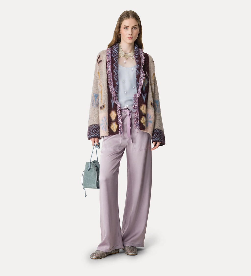 Woman wearing a patterned jacket, light purple pants, and holding a handbag on a white background