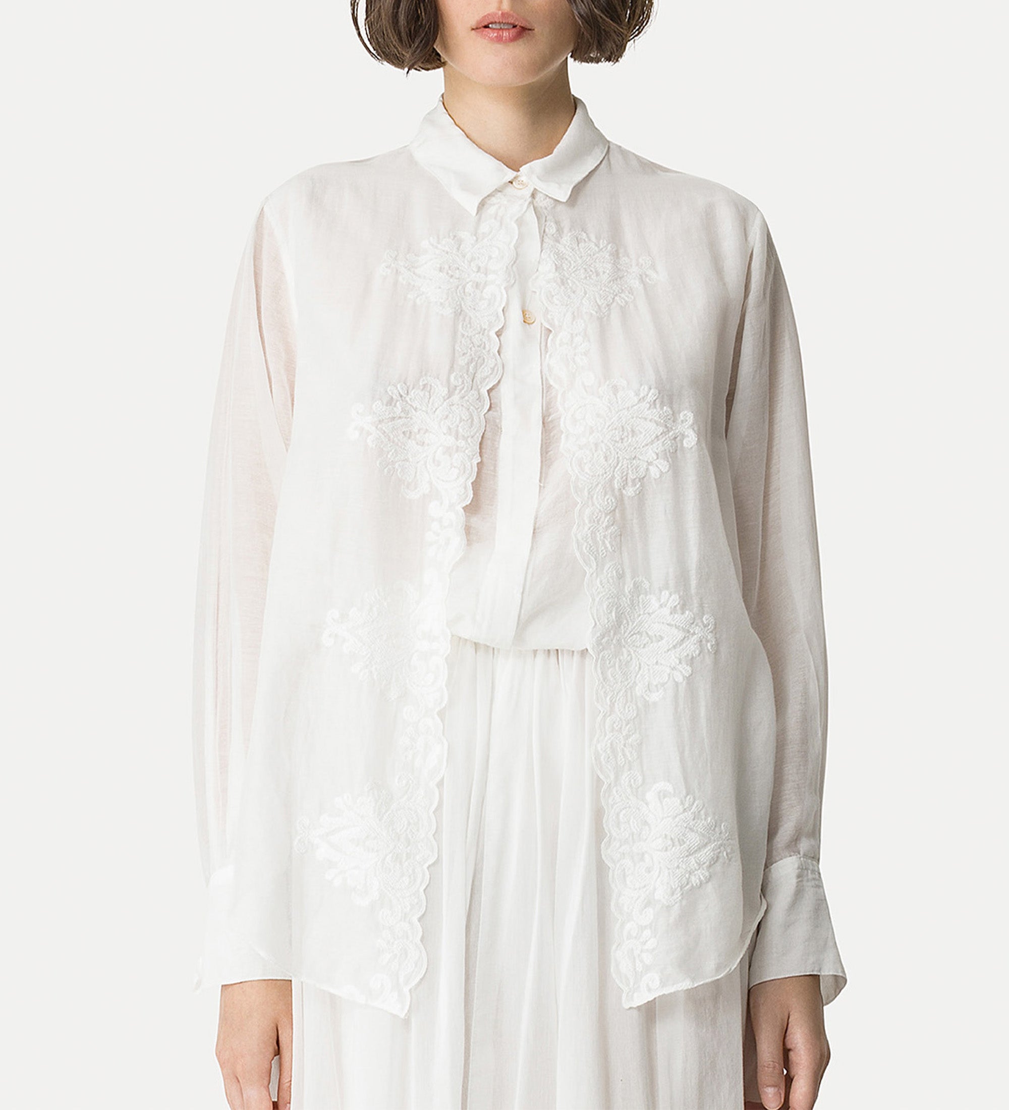 White blouse with floral embroidery worn by a person on a white background