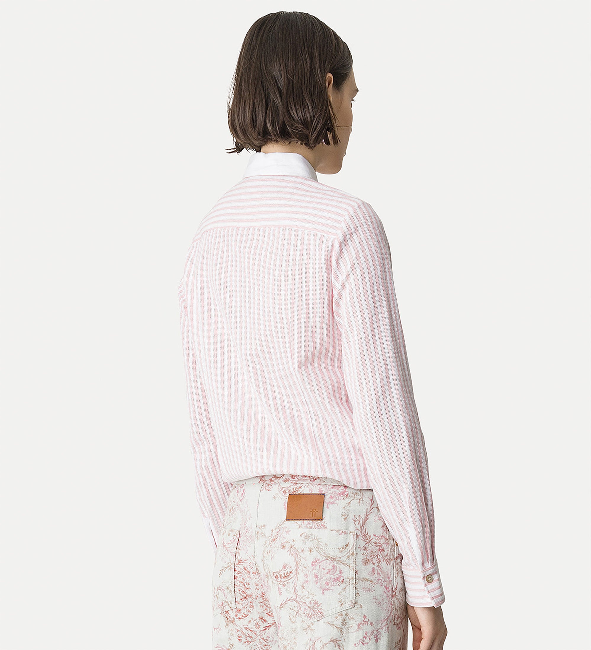 Person wearing a pink striped shirt and floral pants on a white background