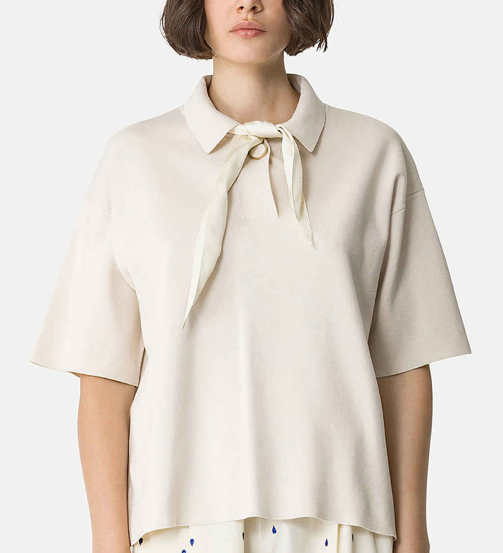 Woman wearing a beige blouse with a bow tie collar on a white background