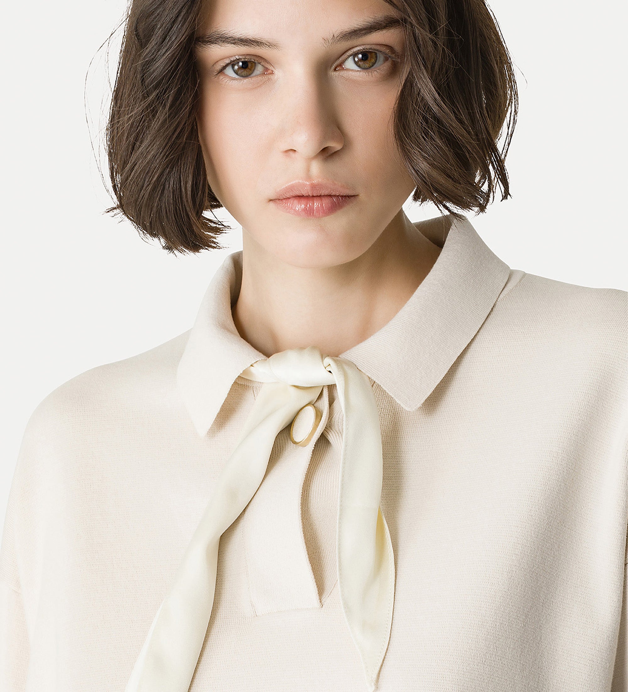 Woman wearing a cream-colored blouse with a necktie detail against a white background