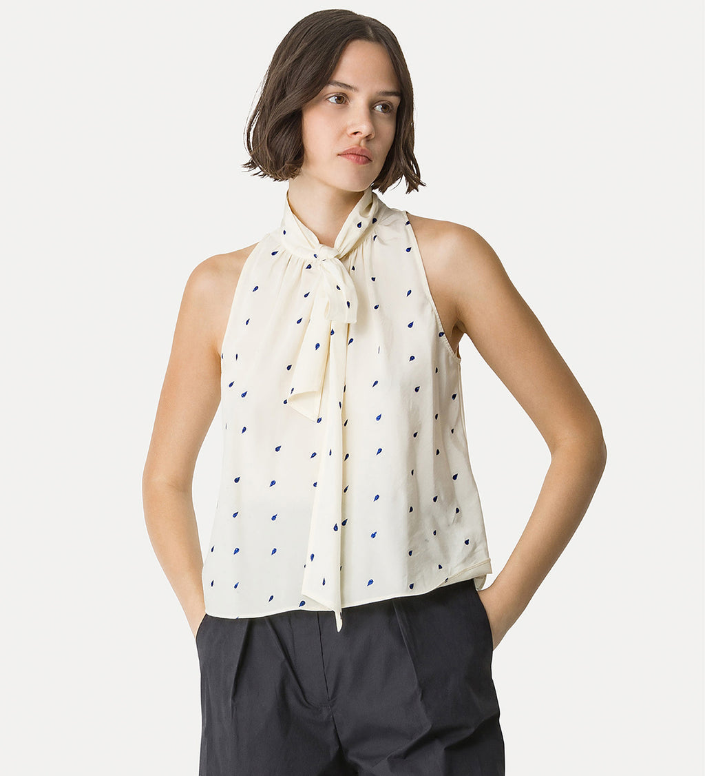 Woman wearing a sleeveless top with a polka dot scarf against a white background