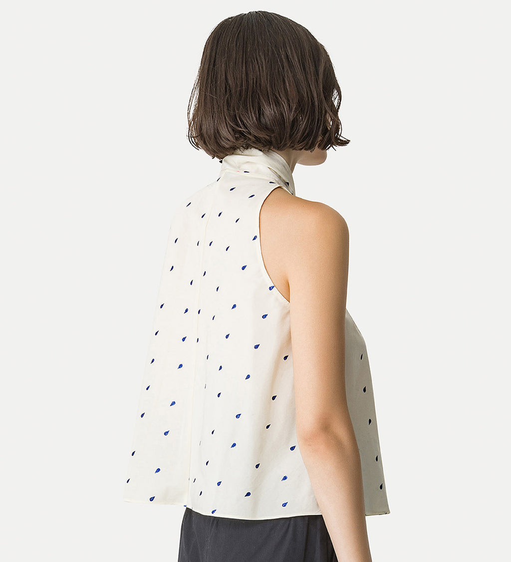 Woman wearing a sleeveless top with a polka dot pattern on a plain background