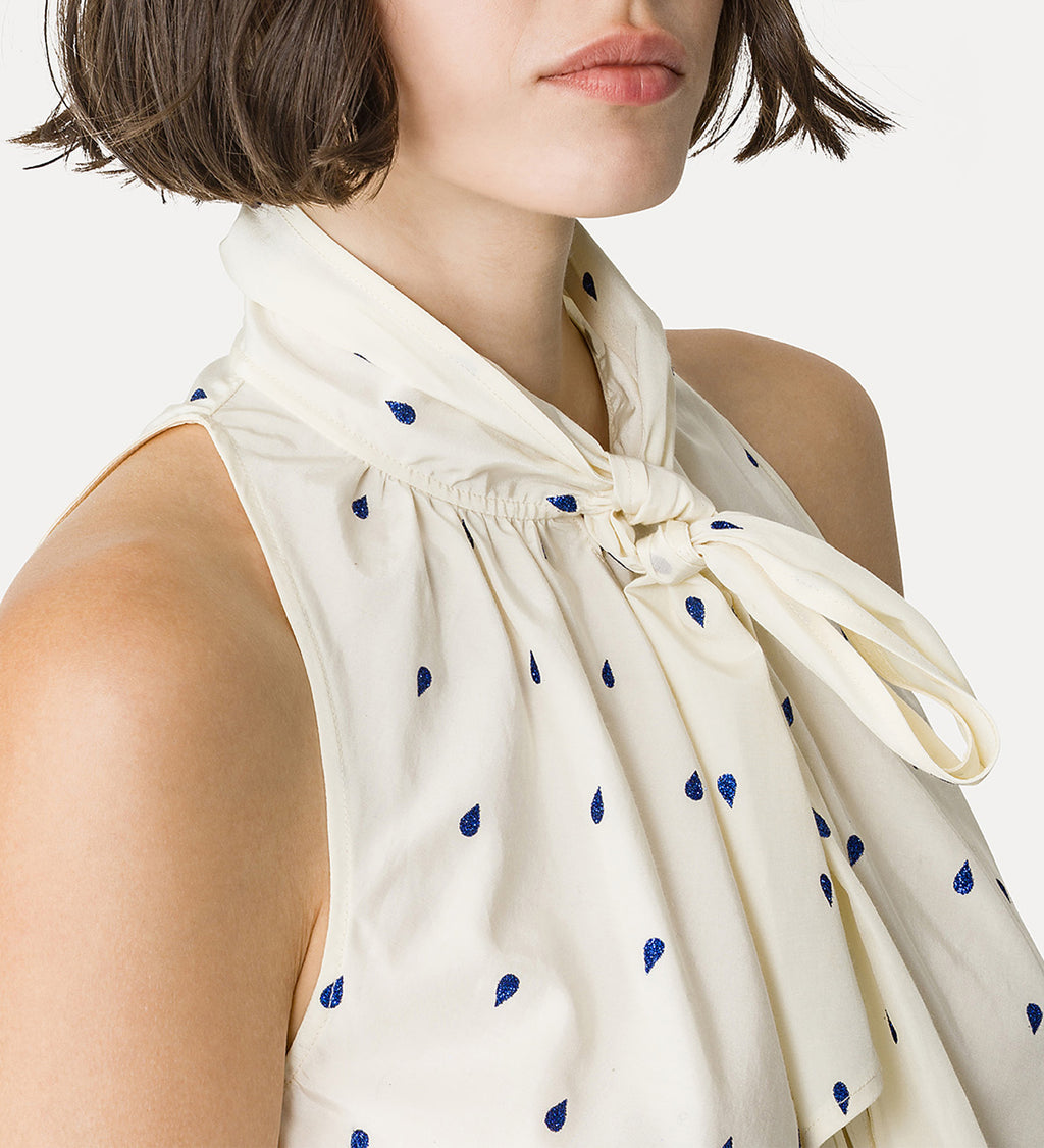 Woman wearing a white sleeveless top with blue polka dots on a white background