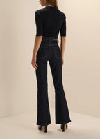 A model shown from the back wearing dark navy blue high-waisted flare jeans and a matching dark navy short-sleeve top, standing against a plain beige studio background.