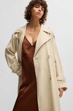 A woman wearing a beige loose-fit double-breasted trench coat with a belt.