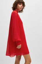 A woman wearing a red high-neck dress with pleated details and sheer sleeves.
