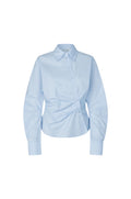 A light blue long-sleeve button-up shirt with a pointed collar and a unique gathered front detail, displayed on a clean white background.