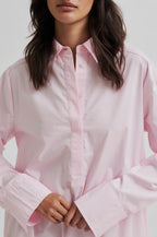 Person wearing a light pink shirt with rolled-up sleeves on a white background