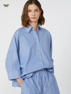 Woman wearing a blue striped shirt and pants on a light gray background