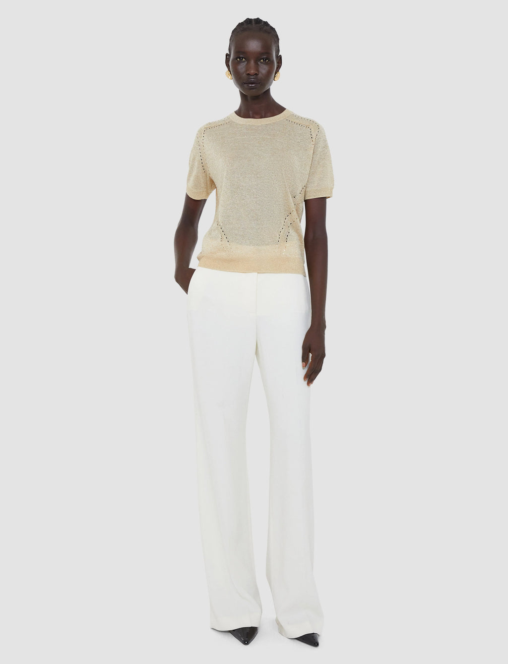 Person wearing a beige knit top and white pants on a light gray background