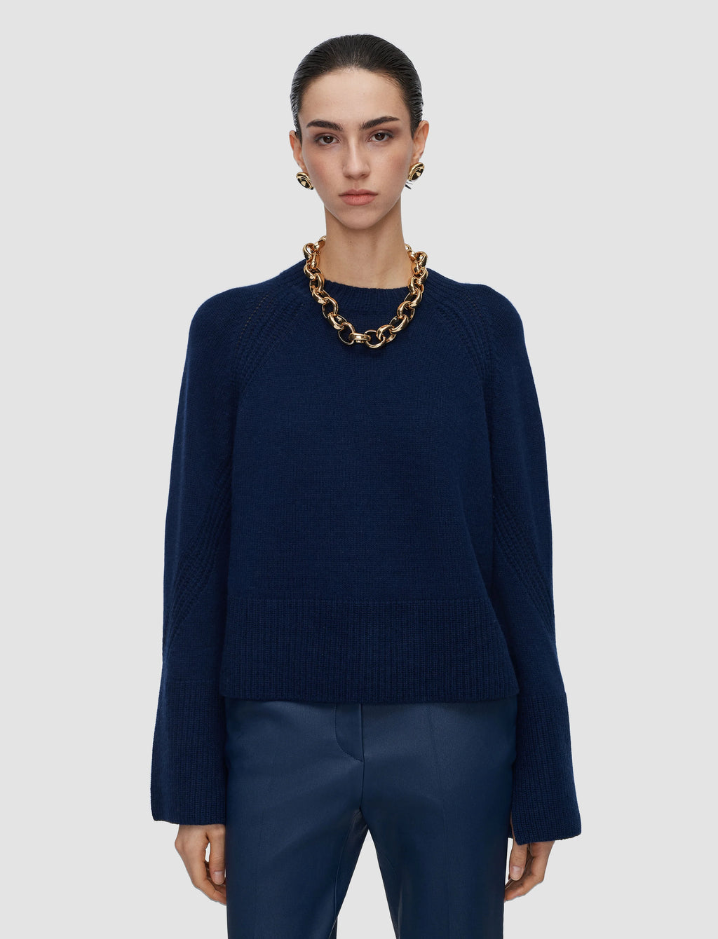 Person wearing a navy sweater and pants with a gold chain necklace on a light gray background