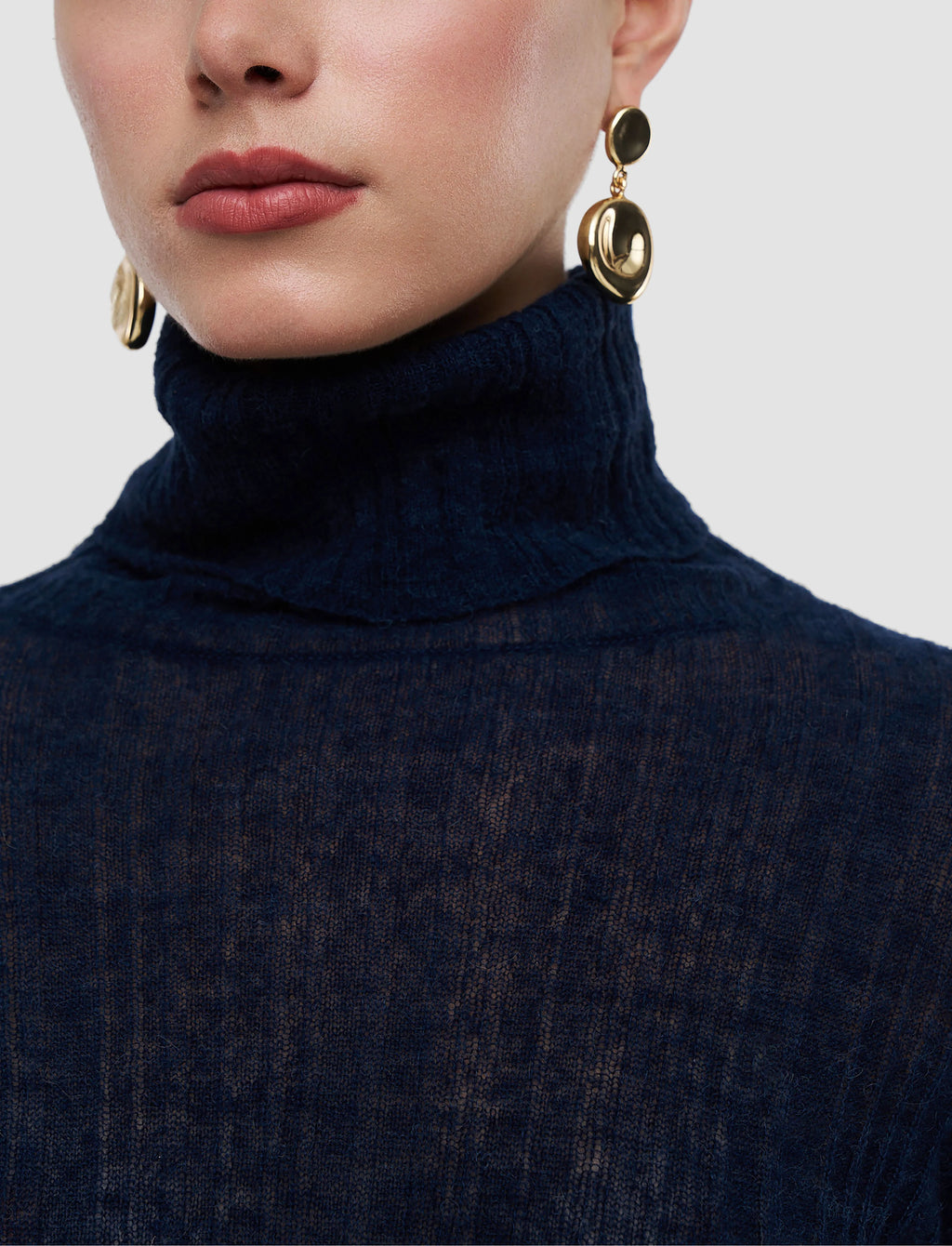 Person wearing a navy turtleneck sweater with gold earrings on a light gray background