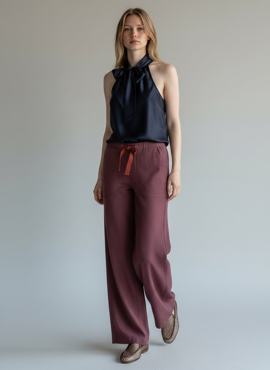 Woman wearing a black sleeveless top and maroon pants against a plain background