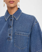 Close-up of a person wearing a blue denim shirt with a collar and pocket.