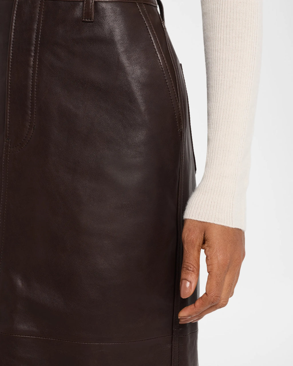 Dark brown leather skirt worn by a person with a white sweater sleeve.
