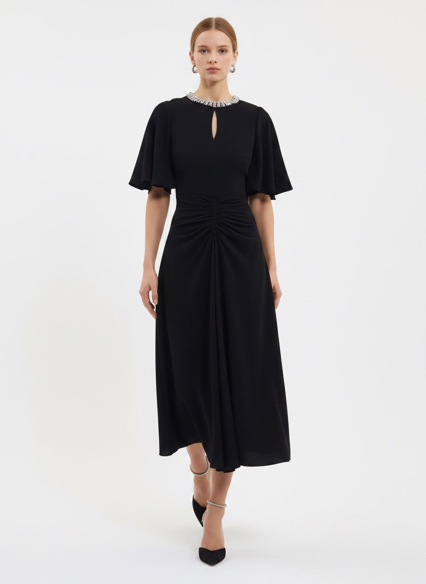 A woman modeling a black midi dress with short flutter sleeves, a keyhole neckline with a pearl-like collar, and a gathered ruched waist, photographed against a plain light gray studio background.